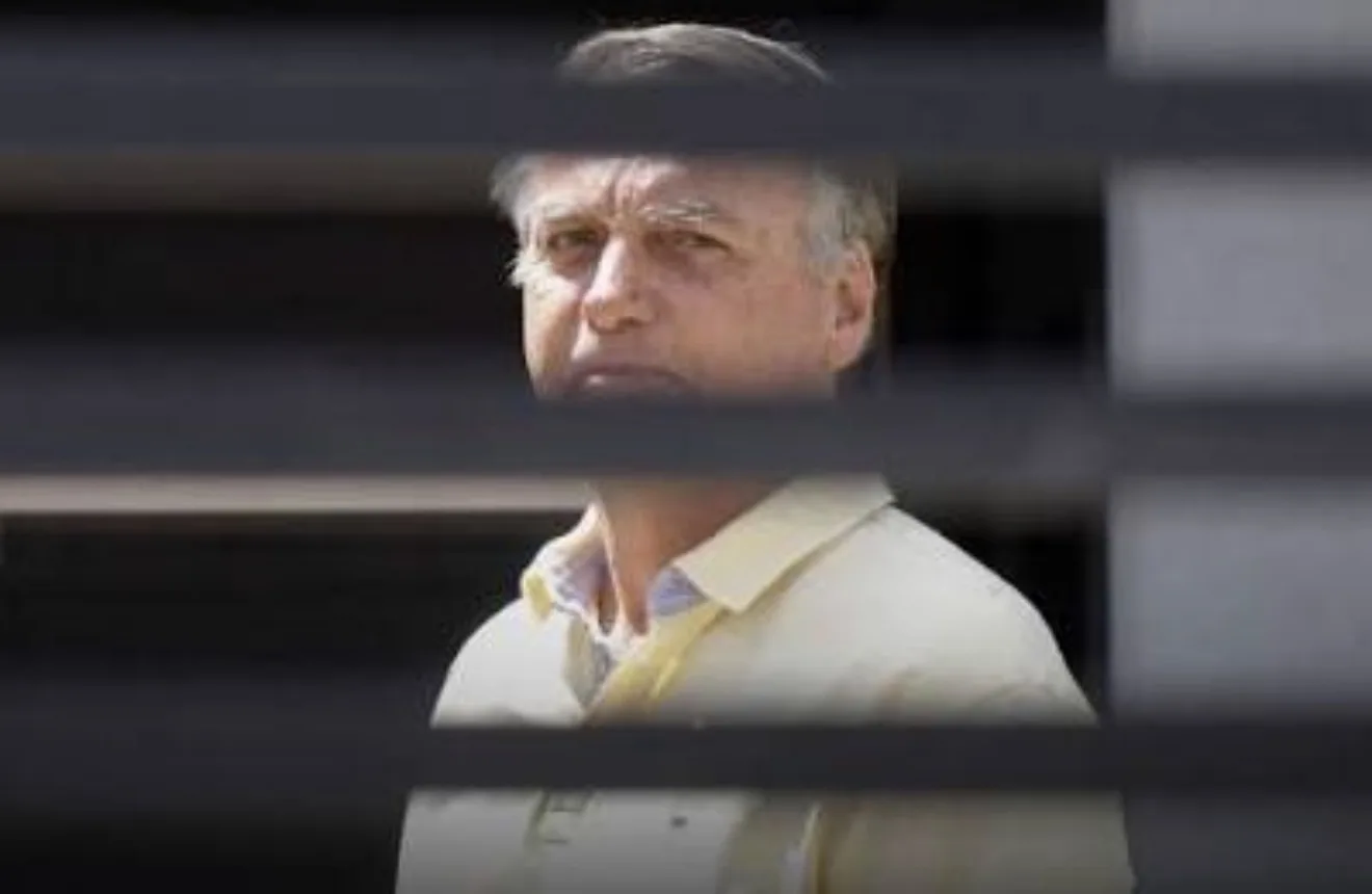 Ex-presidente Jair Bolsonaro em evento oficial com bandeira do Brasil ao fundo.
