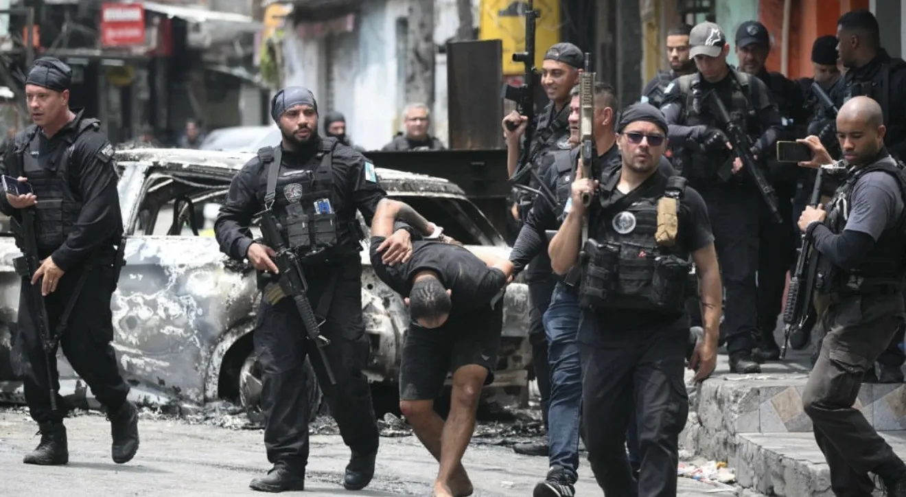 Operação policial contra crime organizado no Brasil com agentes armados e viatura destruída ao fundo