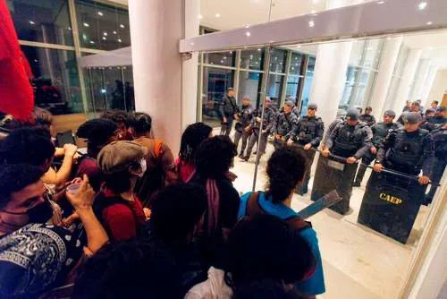 Fachada do prédio da Reitoria da USP em São Paulo com movimentação policial durante o dia.