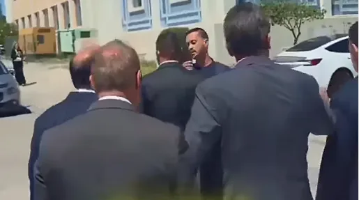 Ministro Gilmar Mendes caminhando cercado por seguranças enquanto o jornalista Sérgio Tavares estende o microfone em Lisboa.