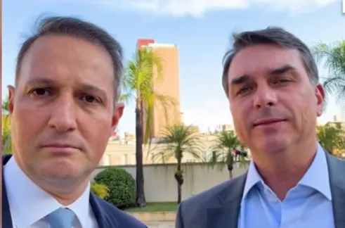 Secretário Guilherme Derrite e o senador Flávio Bolsonaro conversando em ambiente institucional.