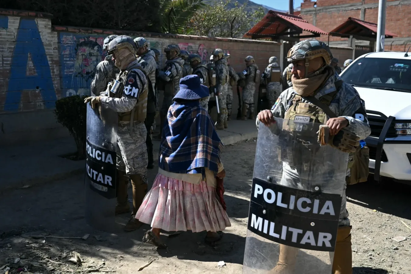 Rodovia boliviana bloqueada com pneus queimados e manifestantes segurando bandeiras nacionais.