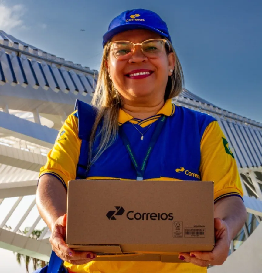 Carteira dos Correios segura uma encomenda diante de uma unidade da estatal