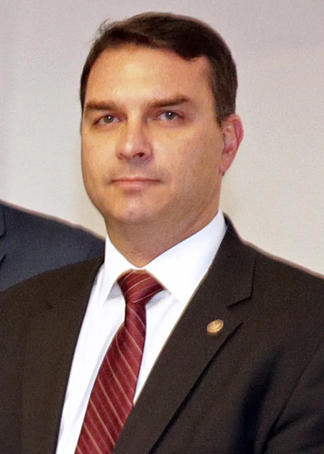 Flávio Bolsonaro de terno escuro e gravata listrada vermelha em retrato formal