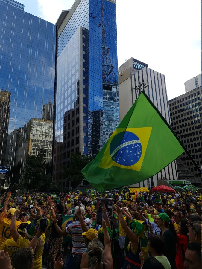 Multidão de verde e amarelo na Avenida Paulista com grande bandeira do Brasil entre os prédios, em ato bolsonarista