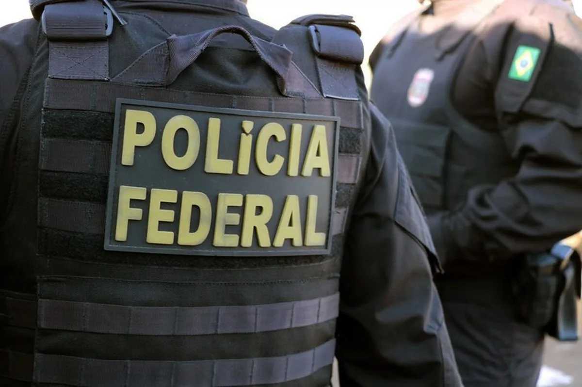 Agentes da Polícia Federal de costas com o patch amarelo POLÍCIA FEDERAL no colete tático