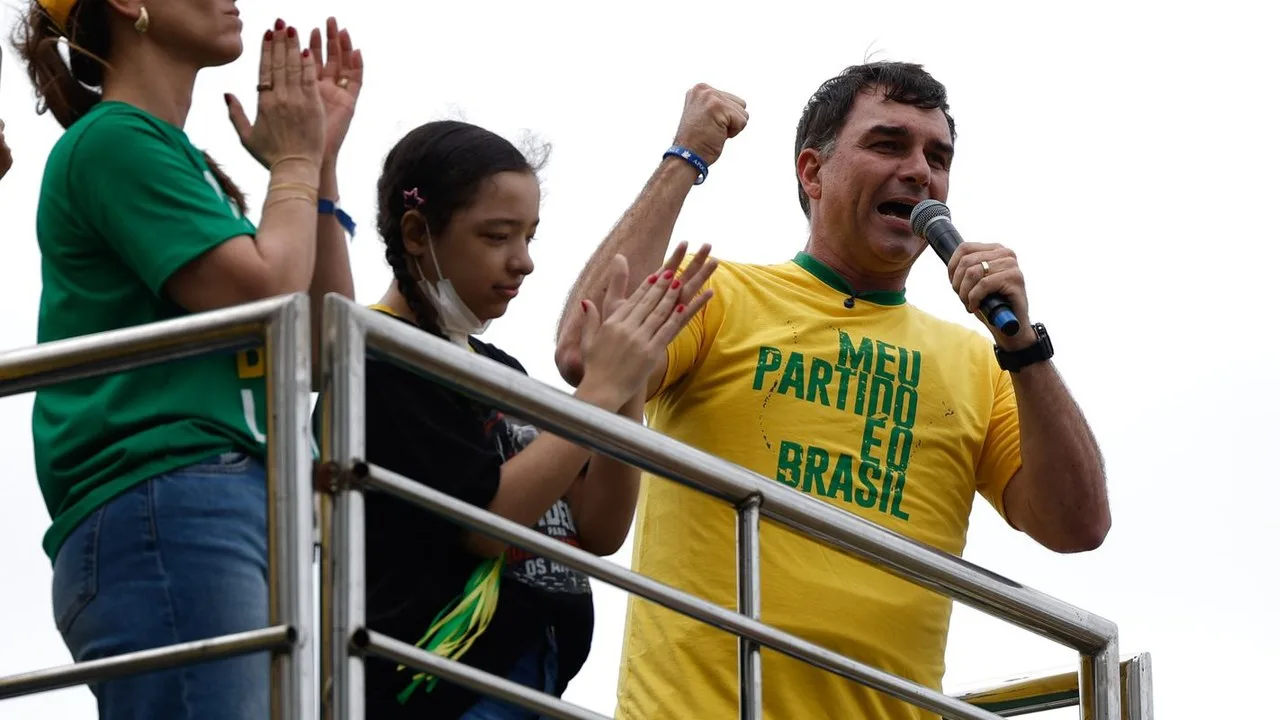 Flávio Bolsonaro em comício de campanha, de camisa amarela, falando ao microfone