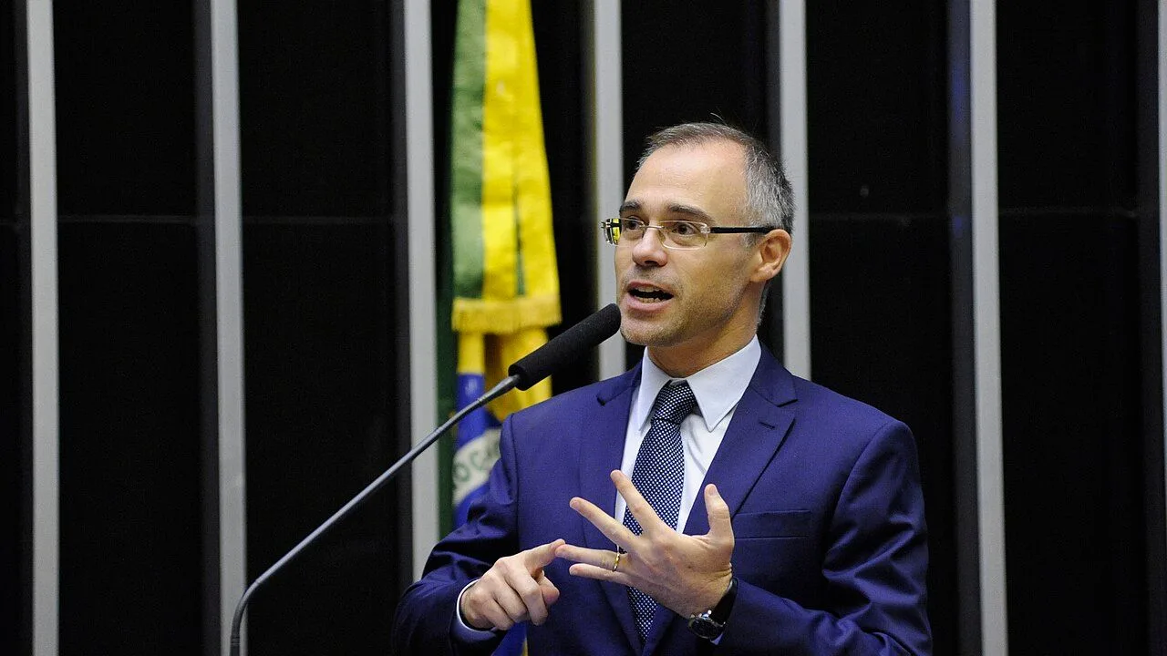 Ministro André Mendonça, do STF, em fala pública com microfone e bandeira do Brasil ao fundo