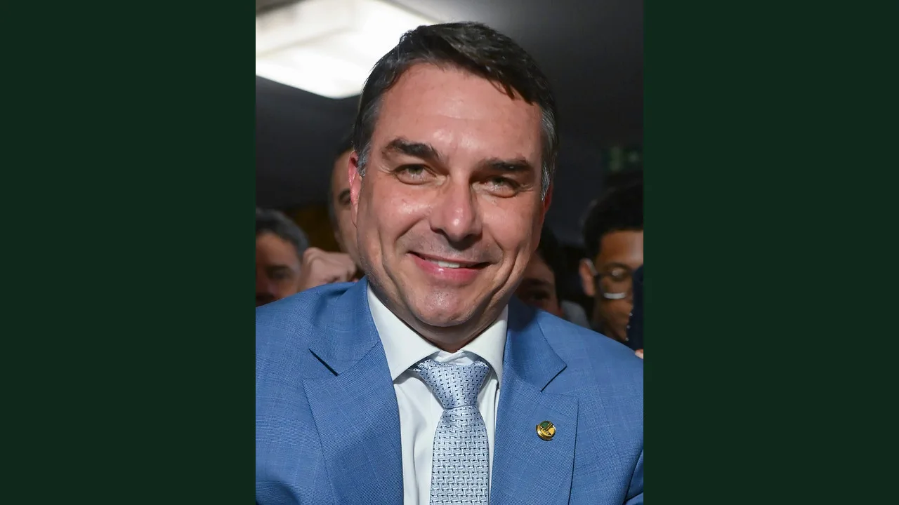 Flávio Bolsonaro sorri, de terno azul-claro, cercado de apoiadores