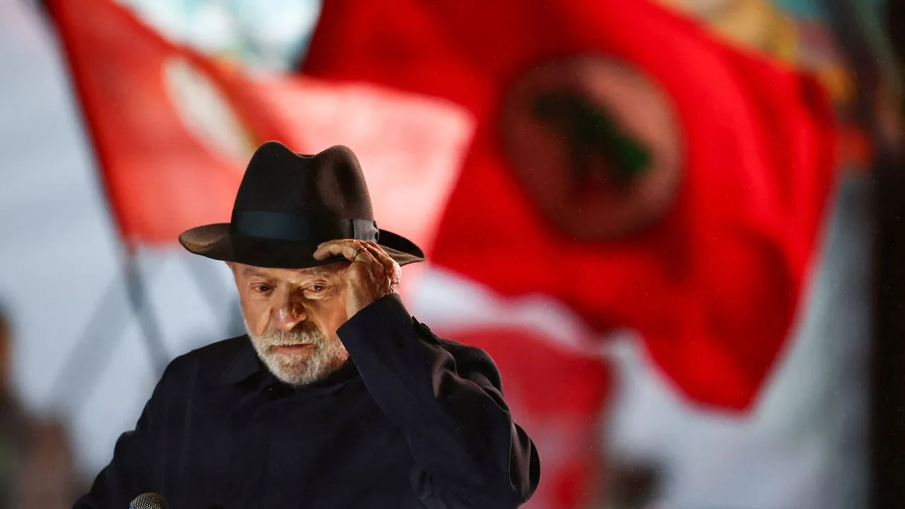 Lula de chapéu em comício com bandeira vermelha ao fundo